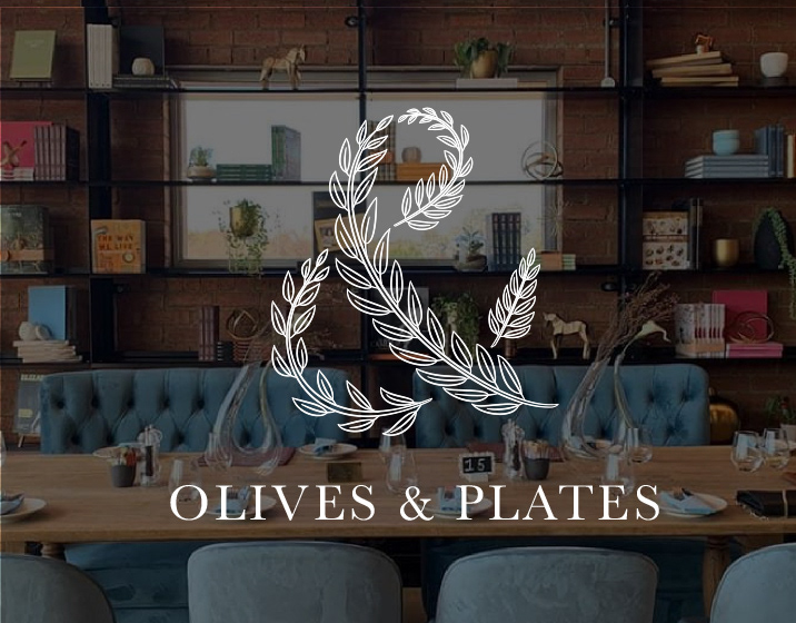 Olives & Plates cafe exterior, Cape-Dutch architecture Wits University, courtyard seating under oak trees, gourmet cakes on display table, chocolate mousse cake under glass dome, Wits campus café lunch, Middle Eastern salad plate, Greek souvlakia dish, red velvet cake slice, peanut butter brittle cheesecake, university staff dining outdoors, Braamfontein hidden gem, casual dining Johannesburg, interior of Olives & Plates café, cake table close-up, Joburg ETC