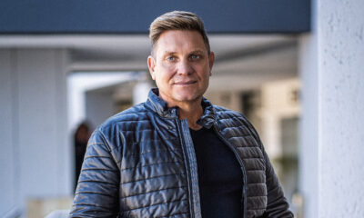 Kurt Darren performing live on stage, tribute concert for Theuns Jordaan in Amsterdam, South African fans attending European music event, Wynand de Villiers speaking about tribute costs, Afrikaans singers performing abroad, Joburg ETC