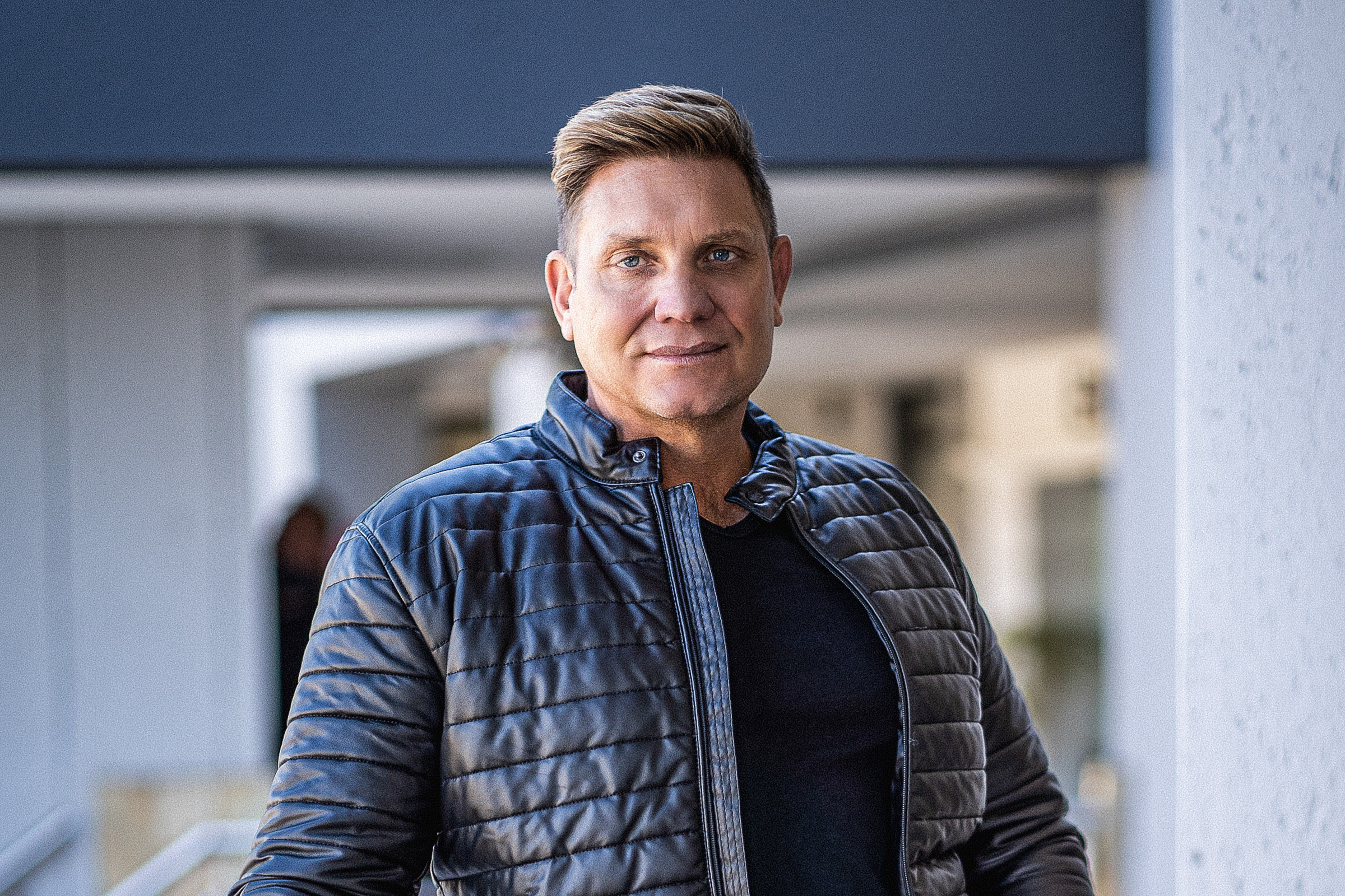 Kurt Darren performing live on stage, tribute concert for Theuns Jordaan in Amsterdam, South African fans attending European music event, Wynand de Villiers speaking about tribute costs, Afrikaans singers performing abroad, Joburg ETC
