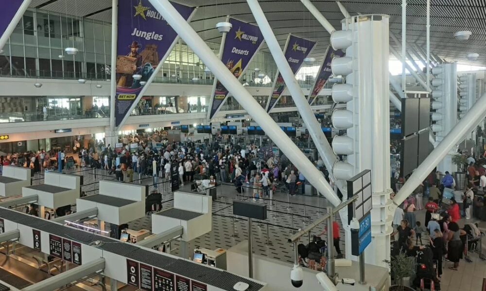 airport departure board showing cancelled flights, stranded traveller with suitcase in terminal, Qatar Airways cancellation message screen, Australian airport waiting area travellers, international flight disruption news, Joburg ETC