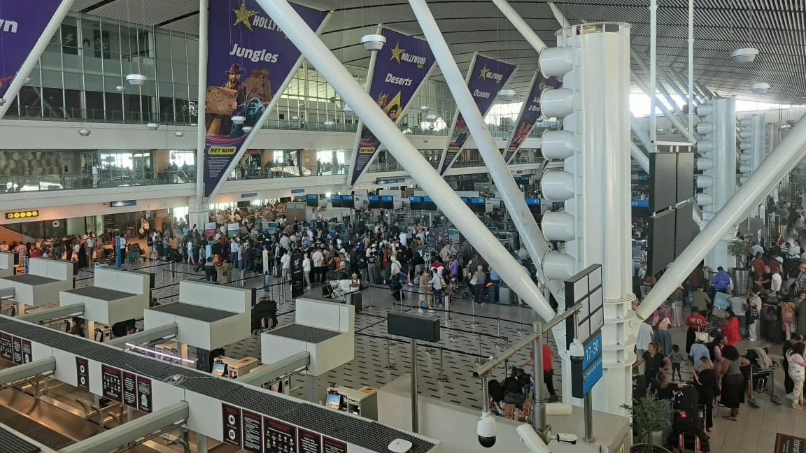 airport departure board showing cancelled flights, stranded traveller with suitcase in terminal, Qatar Airways cancellation message screen, Australian airport waiting area travellers, international flight disruption news, Joburg ETC
